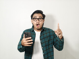 Adult man showing shocked expression with finger pointing up when holding mobile phone isolated on white background