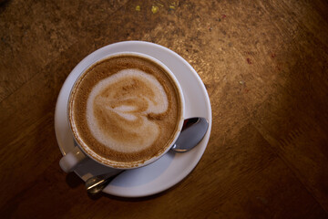 Top view of a cappuccino with a heart-shaped latte art design on the froth, placed on a wooden table.