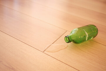 Green glass bottle spills liquid on light wooden floor