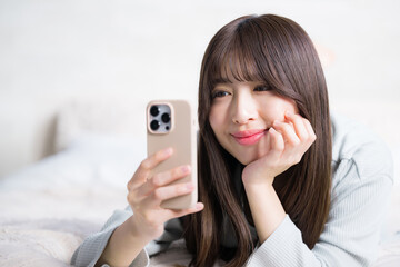 ベッドで寝転んでスマホでを持つ笑顔の女性