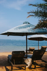 A large umbrella with two wooden sun loungers on the beach with the ocean in the background. Places to relax by the sea
