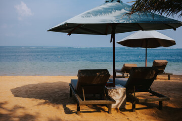 A large umbrella with two wooden sun loungers on the beach with the ocean in the background. Places to relax by the sea