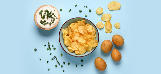 Bowl of tasty sour cream with sliced green onion and potato chips on blue background