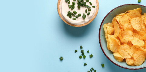 Bowl of tasty sour cream with sliced green onion and potato chips on blue background