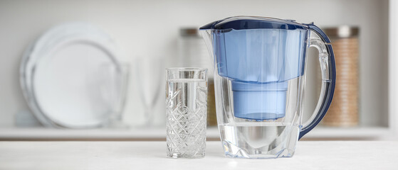 Water filter jug with glass on table in kitchen
