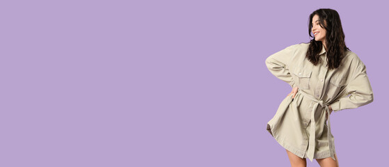 Happy young woman in stylish dress dancing on lilac background