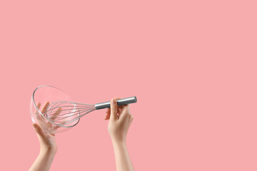 Female hands holding whisk and glass bowl on pink background