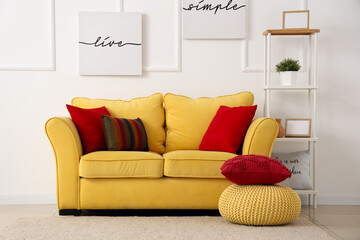 Yellow sofa with cushions and pouf near white wall