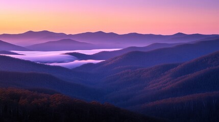 Fototapeta premium Serene sunrise over misty mountain range, showcasing layers of purple and pink hues.