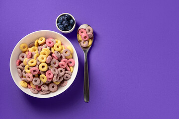 Bowls with colorful sweet cereal rings and blueberries on purple background
