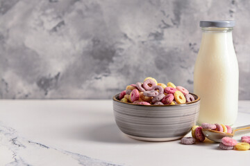 Bowl with colorful sweet cereal rings and bottle of milk on white table