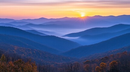 Obraz premium Majestic sunrise over layered blue mountains, showcasing autumn foliage and misty valleys.
