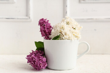 Cup with blooming lilac flowers on white background