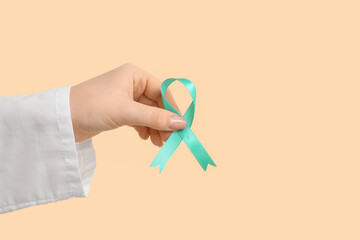 Female doctor hand with turquoise ribbon on beige background. Cervical Health Awareness Month