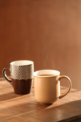 Mugs of hot tea on wooden table against brown background
