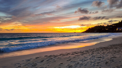 Obraz premium Golden sunset over the ocean with waves washing up on the sandy shore, reflecting warm colors of the sky. Seychelles, Mahe.