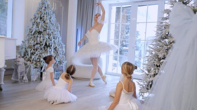 Group of young girls are dressed in white and are dancing in front of a Christmas tree. Scene is festive and joyful, as the girls are dressed in traditional ballet attire