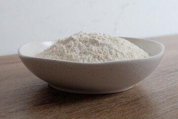 Flour in a white stone bowl with a white and wood background