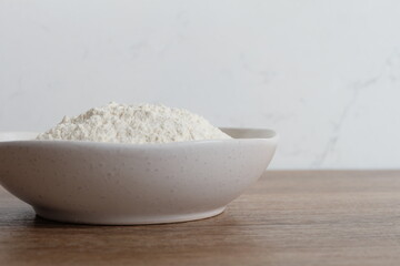 Flour in a white stone bowl with a white and wood background