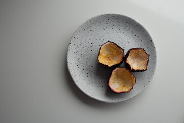 3 peeled passionfruit shells on a spotted white and black plate with a grey stone table background