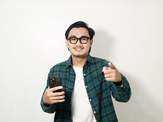 happy asian man is holding mobile phone while pointing to camera isolated on white background