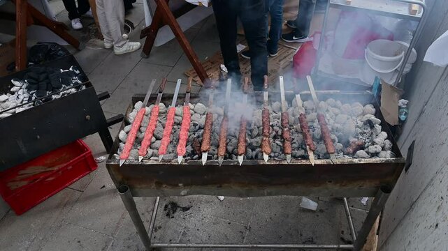 Chef grilling kofta skewers on a charcoal grill in a food booth in the street during daytime