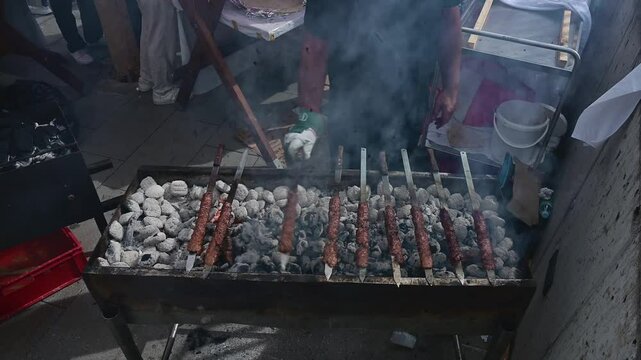 Chef grilling kofta skewers on a charcoal grill in a food booth in the street on a sunny day