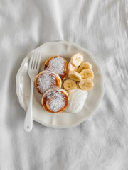 Syrniks with greek yogurt, honey and banana on a light background, top view
