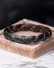 Braided green stone bracelet on a velvet cushion.