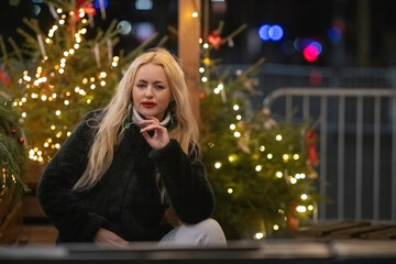 Portrait of a young beautiful blonde girl in a dark fur coat in the night city.