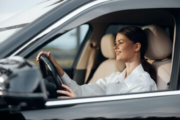 A woman in the driver's seat of a car with her hand on the steering wheel, looking directly at the camera, capturing a moment of confidence and control in a modern vehicle