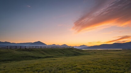 Fototapeta premium grassy field with fence and fenced in area with mountains in background
