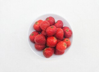 Close-up of strawberries in a small white plate on a white background. 