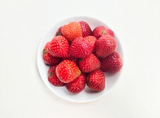 Close-up of strawberries in a small white plate on a white background. Top of view. 
