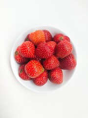 Strawberries in a small white plate on a white background. Top of view. 