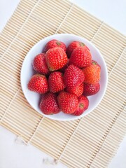 Strawberries in a small white plate on a white background. Top of view. 