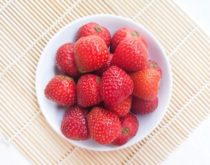 Close-up of strawberries in a small white plate on a white background. Top of view. 