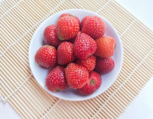 Close-up of strawberries in a small white plate on a white background. Top of view. 