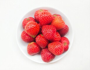 Close-up of strawberries in a small white plate on a white background. 