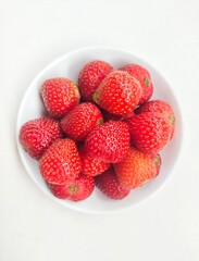 Close-up of strawberries in a small white plate on a white background. 