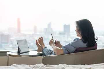 Work-Life balance, life quality, work and travel concept with Asianbusiness woman relaxing, take it easy resting in modern city hotel guest room or luxury home living room with computer and smartphone