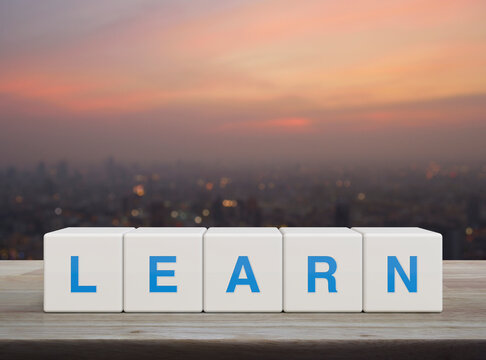Learn letter on white block cubes on wooden table over blur of cityscape on warm light sundown, Business, education and learning concept