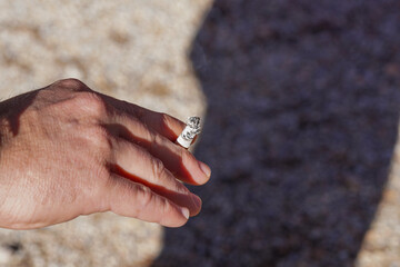 hand of a person, holds a cigar in the park, close-up on brown ground background