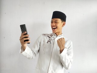 Moslem Asian man clenched fist showing excitement when looking to his mobile phone