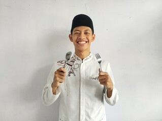 Moslem Asian man smiling happy with hand holding dinning spoon and fork