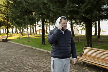 Fototapeta premium Man talking on the phone in a city park, sitting on a bench holding a smartphone, engaging in a conversation outdoors.