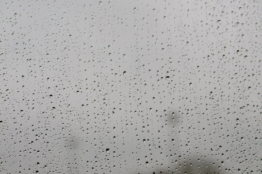 Raindrops on window glass against the moody grey British sky create a natural pattern. Water droplets on a transparent surface capture the minimalist texture during typical overcast weather