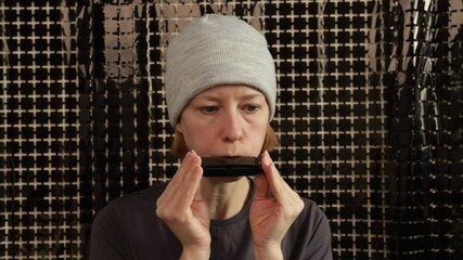 Harmonica lessons, woman playing musical instrument at home, silver harmonica practice in studio setting, leisure activity focused on musical skill.