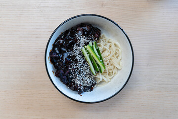 A bowl of black bean noodles with cucumber.