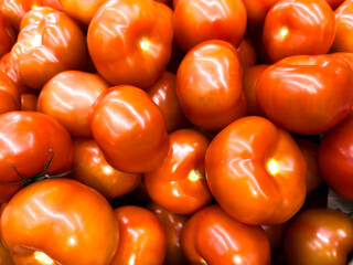 Fresh, ripe tomatoes piled together in a grocery store, showcasing their vibrant orange color and smooth texture